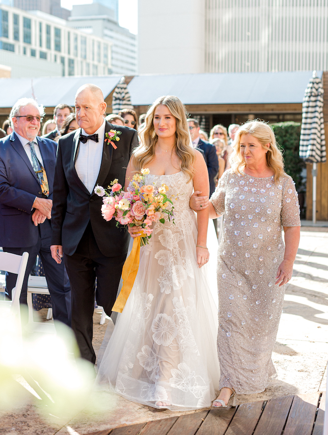 The bride walking down the aisle with both of her parents by her side. 