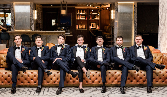 The groom and groomsmen sitting on a brown leather couch at the Four Seasons Hotel Houston.