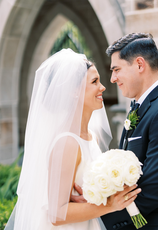 The bride and groom smiling at each other while the bride is holding a white bouquet.