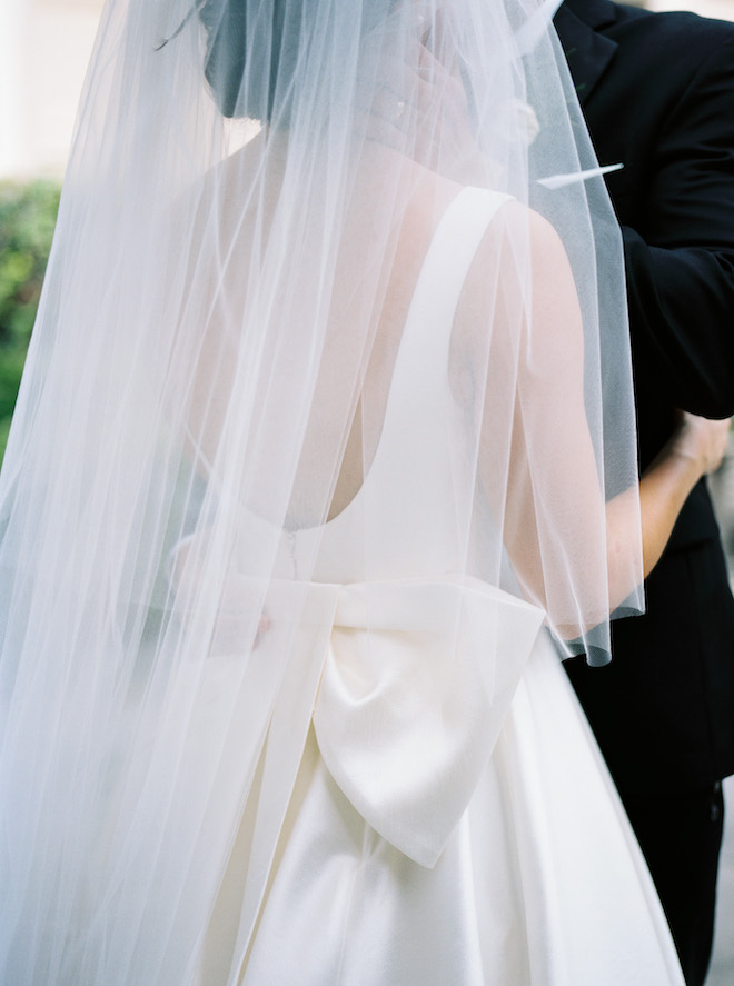 The back of the bride's dress with a big bow and her veil draping over it.