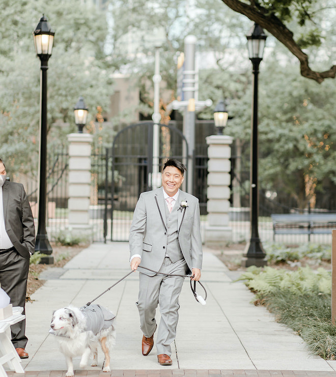 The groom and his dog walking to the wedding ceremony in matching suits.