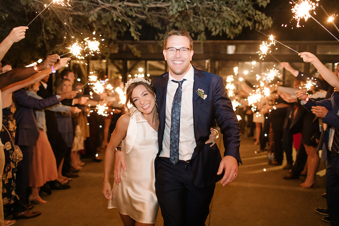 The bride and groom smiling as they leave their autumn wedding reception, while their guests give them a sparkler send off. 