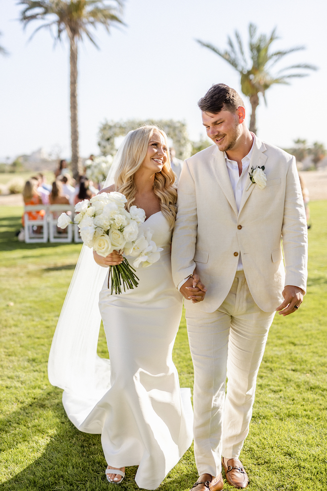 The bride and groom holding hands and smiling as they leave their wedding ceremony.