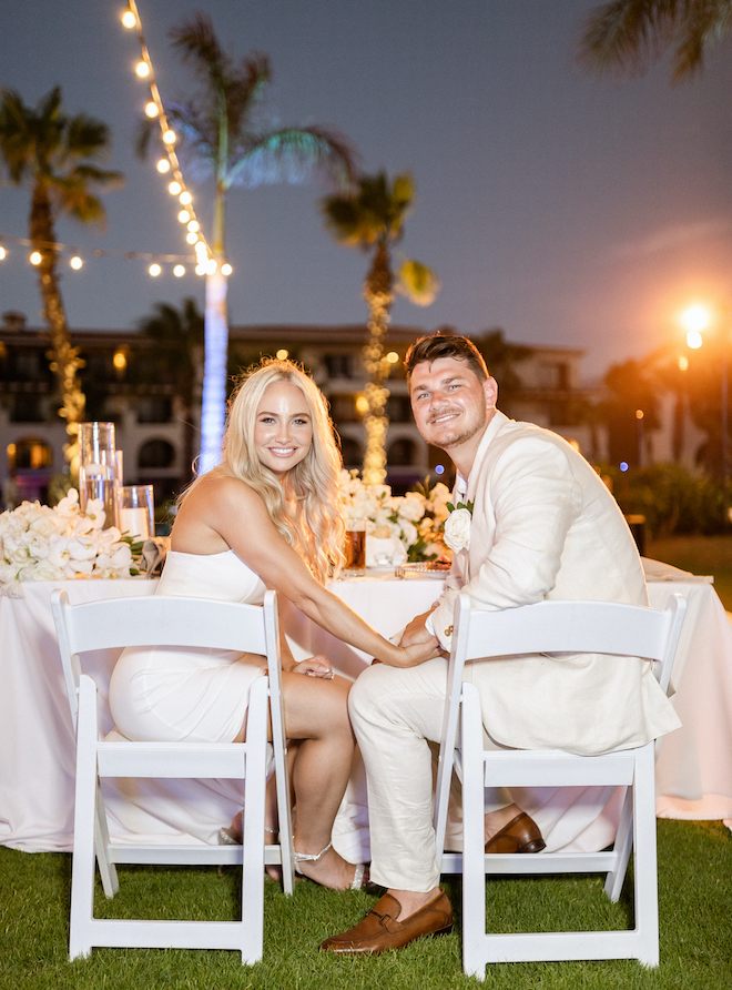 The bride and groom seated at their table smiling.