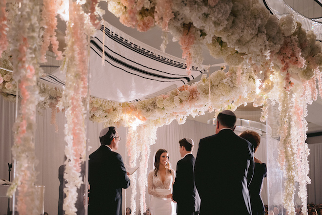 The bride and groom during their ceremony underneath a floral-filled altar at their opulent ballroom wedding.