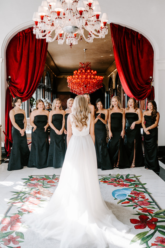 The bridesmaids in black dresses smiling at the bride's reveal.