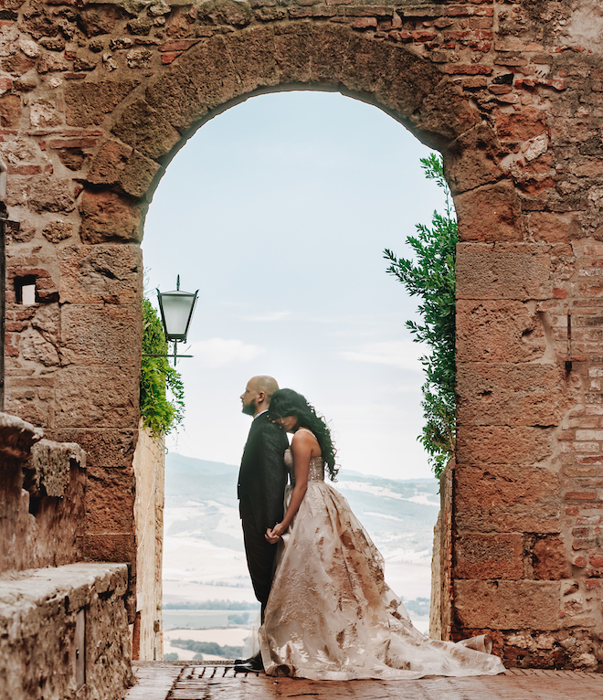 The bride and groom stand under a stone arch for their Italian wedding featured in the Weddings in Houston magazine. 