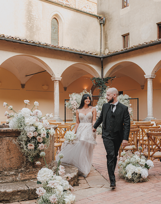 The bride and groom smiling and holding hands at their ceremony space.