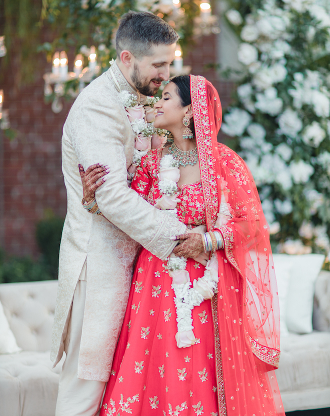 The bride wearing a red lehenga while hugging the groom.