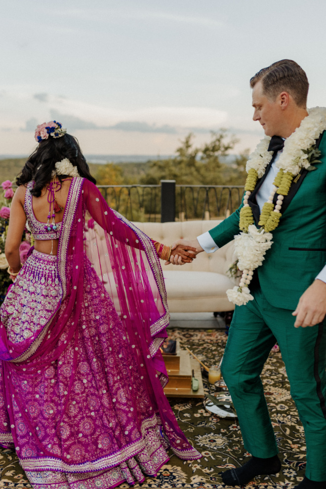 The bride and groom hold hands as they participate in a Hindu wedding ceremony ritual.