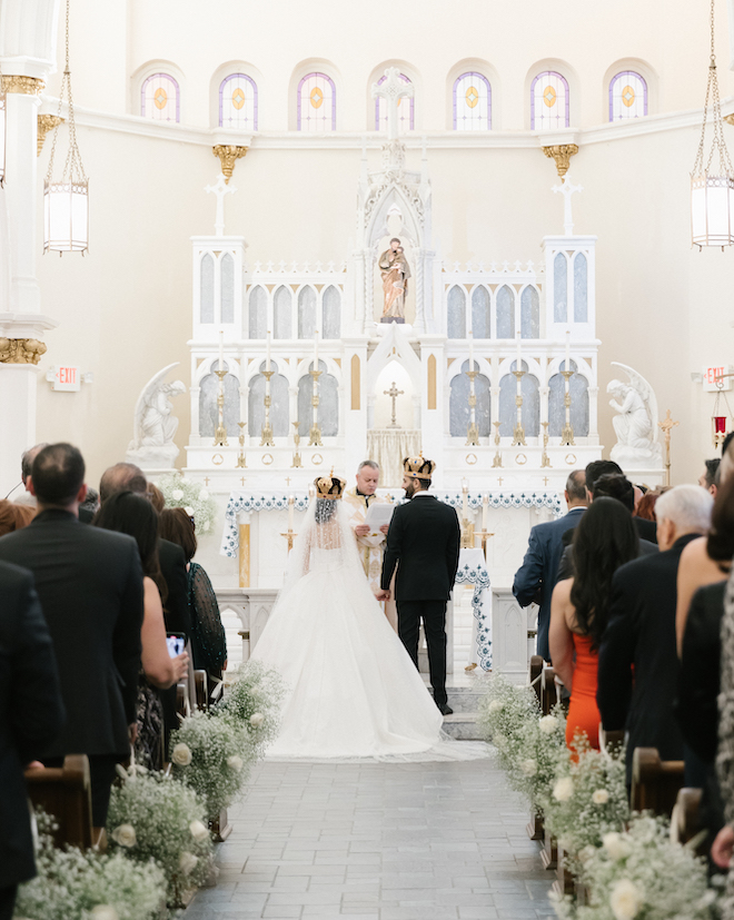 The bride and groom wearing crowns at the altar.