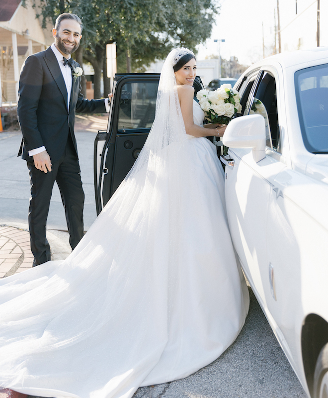 The bride getting into a white car as the groom holds the door for her.