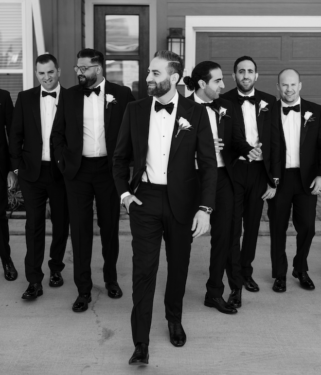 The groom and his groomsmen walking in front of a house.