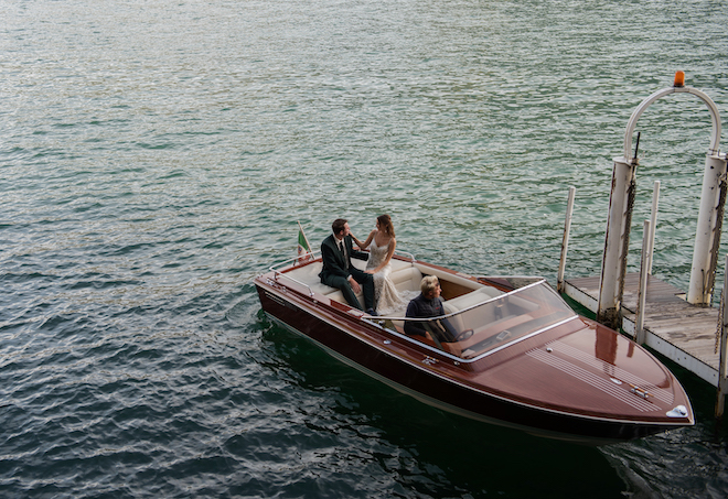 The bride looking at the groom with her hand on his shoulder while sitting in a boat.