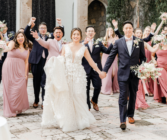 The bride and groom holding hands as the wedding party cheers behind them.