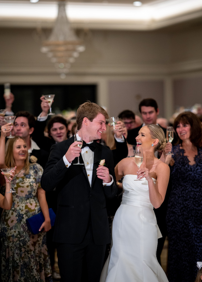 The bride and groom smiling as they hold champagne during a toast.