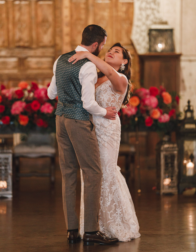 The bride and groom dancing with vibrant pink and orange flowers behind them.