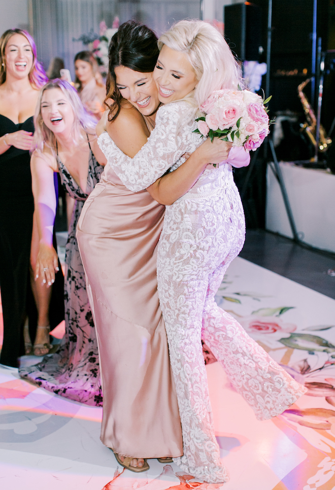 The bride and a bridesmaid hugging on the dance floor. 