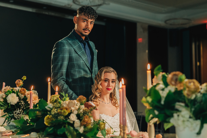 Groom standing behind the bride with flowers and candlelight decorating the table.