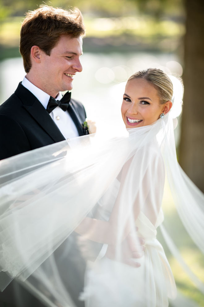 The groom smiling at the bride as her veil flows in the wind.