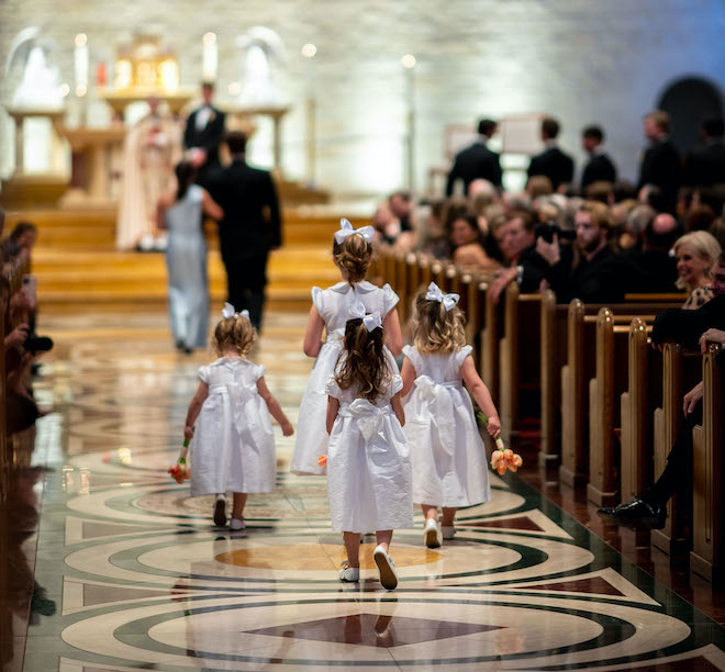 Four flower girls in white dresses walking down the aisle.