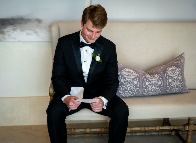 The groom smiling as he reads a letter from the bride.