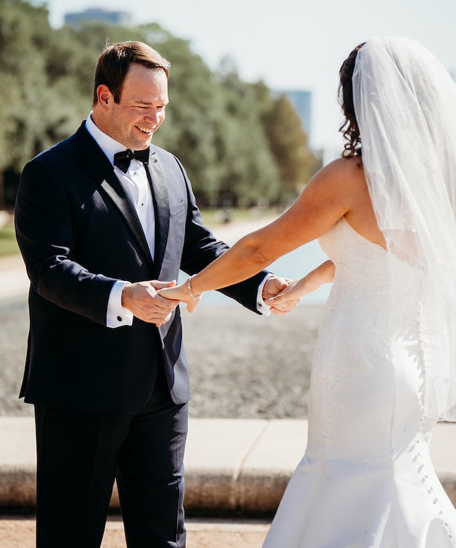 The groom smiling at the bride and holding her hands during the first look.