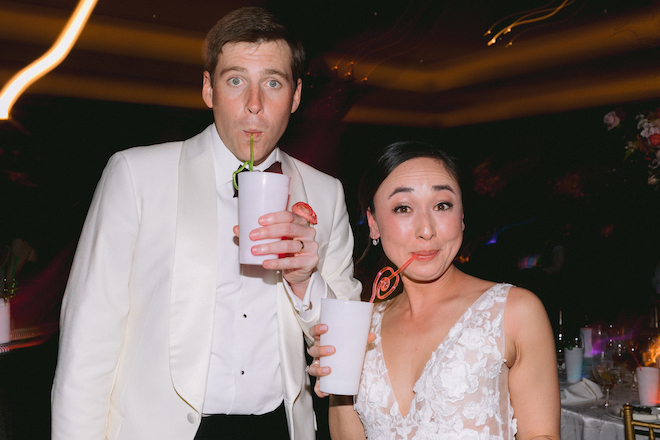 The bride and groom sipping out of white cups with swirly straws. 