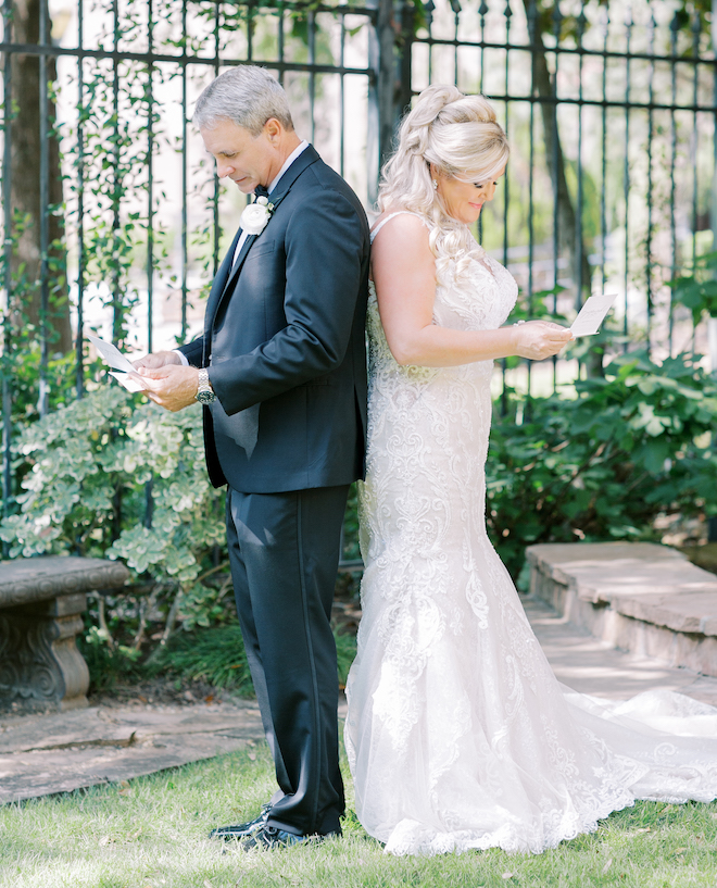 The bride and groom standing back-to-back reading letters to each other. 