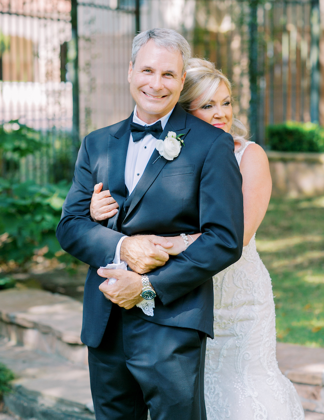 The bride hugging the groom from behind and the groom smiling. 