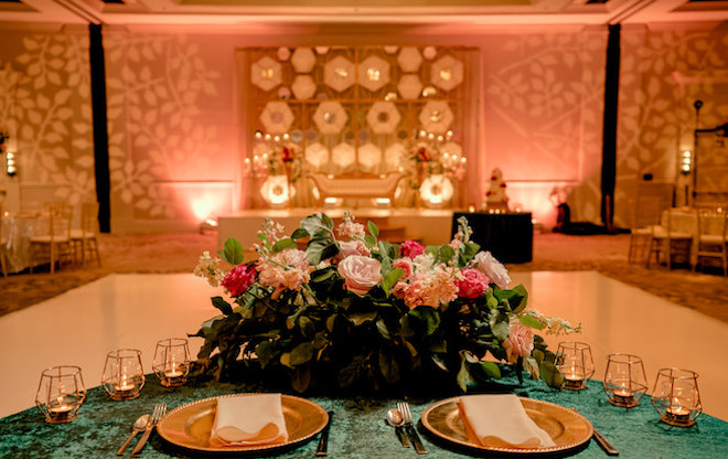 A reception table decorated with gold chargers, florals and candles overlooking the dance floor.