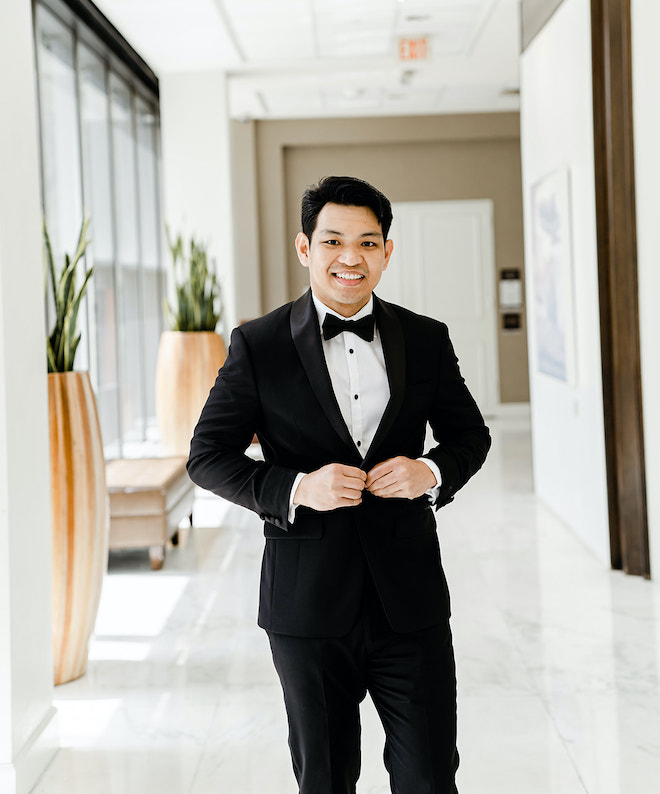 The groom smiling as he buttons his tux.