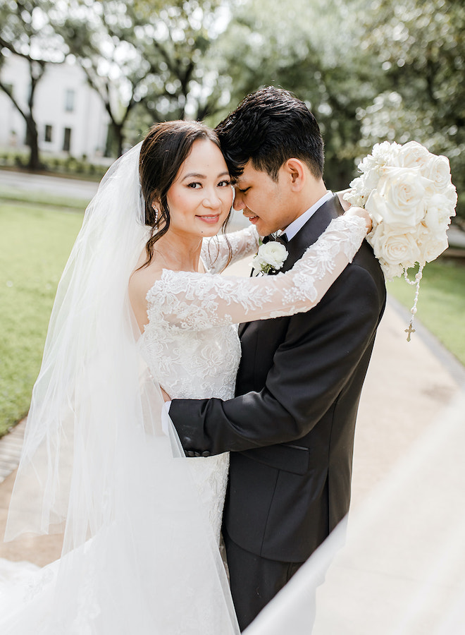 The bride smiling as she hugs the groom.