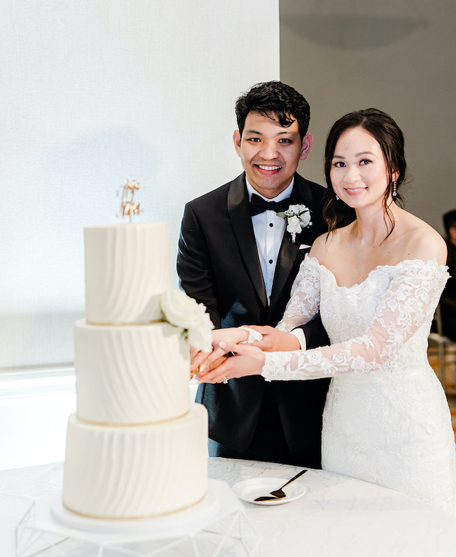 The bride and groom cutting into their white and champagne colored wedding cake.