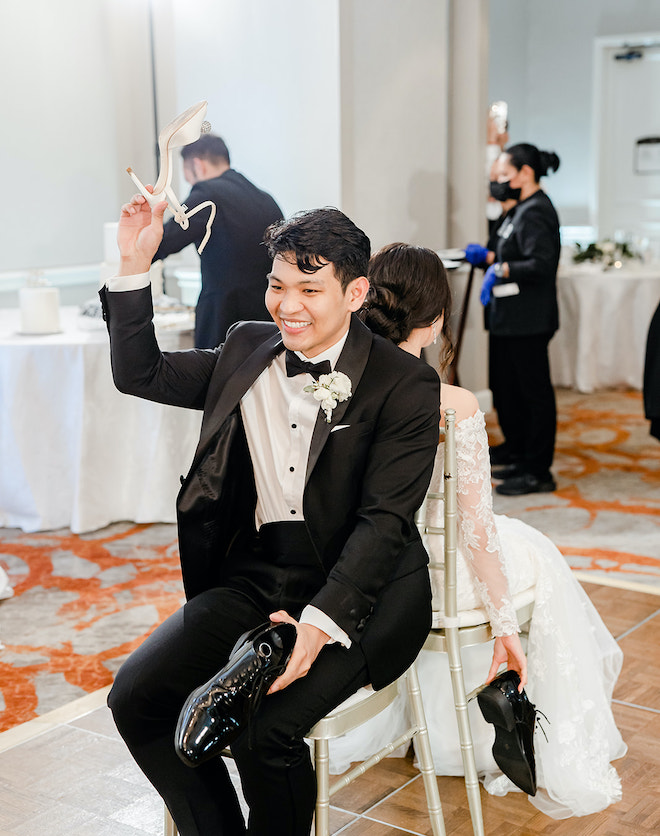 The bride and groom sitting as they hold each others shoes in the air.