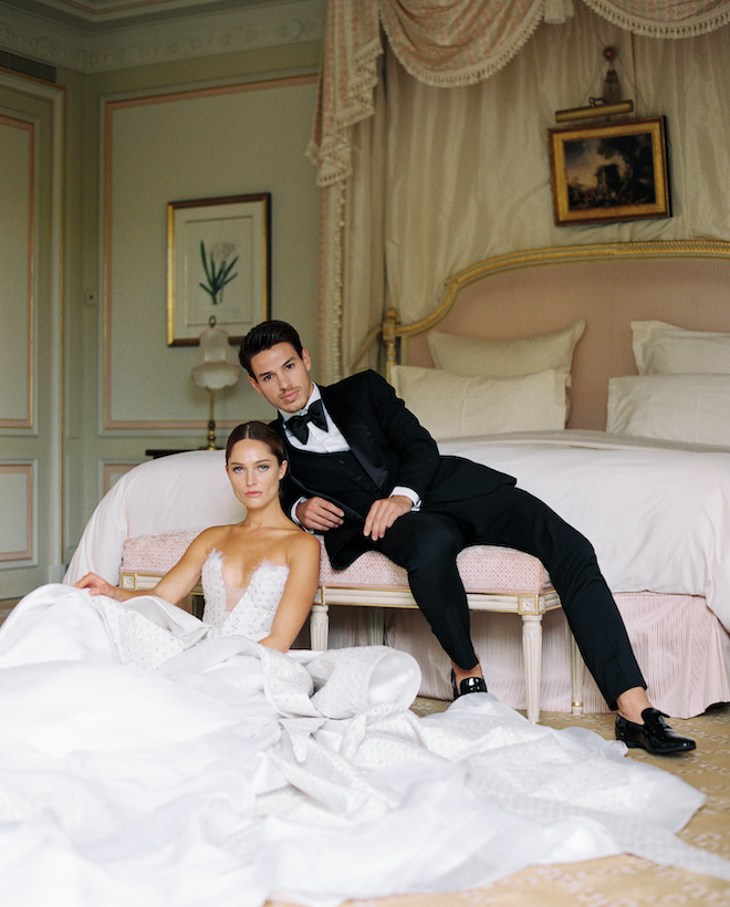 The groom resting on a bench as the bride sits on the floor of a pink and green bedroom.