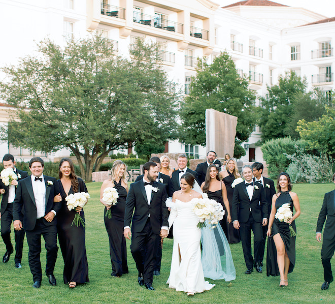 The bride and groom holding hands as their wedding party walks behind them at their wedding in the San Antonio hill country.