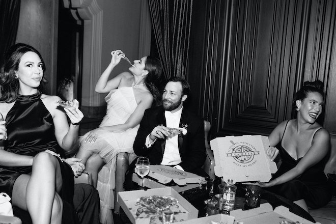 The bride, groom and guests smiling and eating pizza.