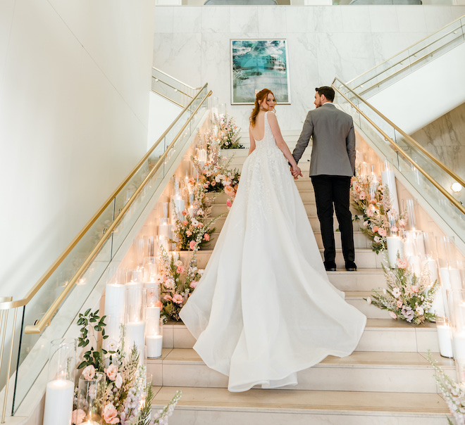 The bride and groom holding hands on the grand staircase of The Laura Hotel.