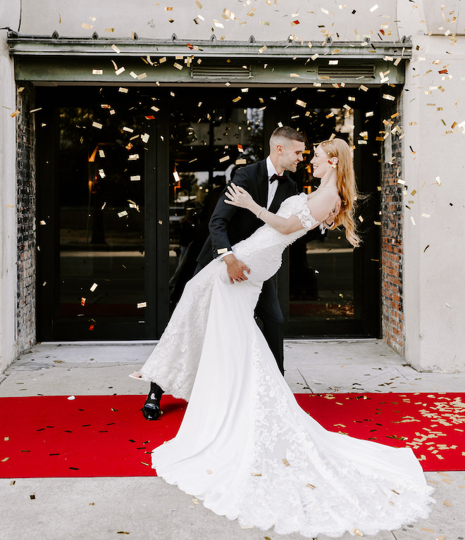 A groom holding the bride as gold confetti surrounds them outside the Vault at Corinthian Houston.