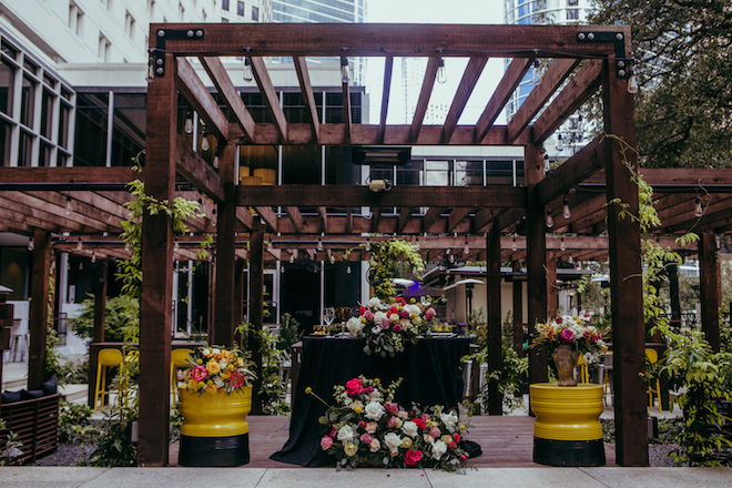 Outdoor dining area with a table set with florals and dining settings underneath a pergola at wedding venue, Whitehall Houston.