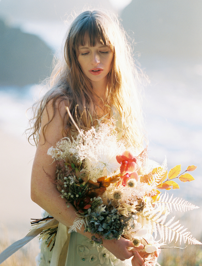 The bride looking down at a bouquet of warm-hued florals.