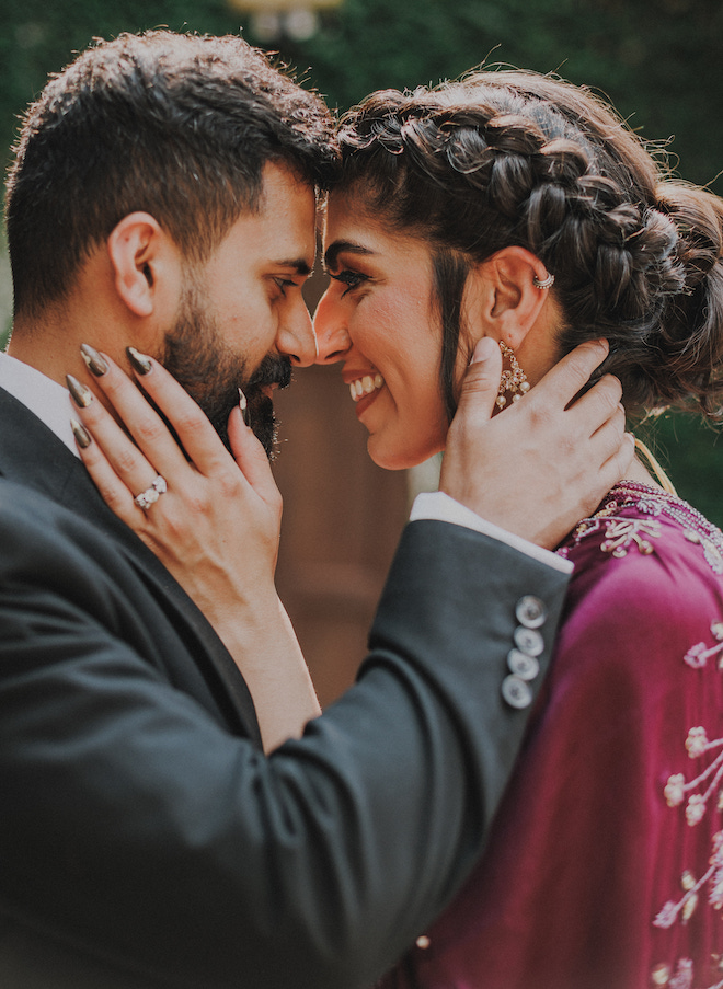 The bride and groom smiling at each other with their hands on their faces.