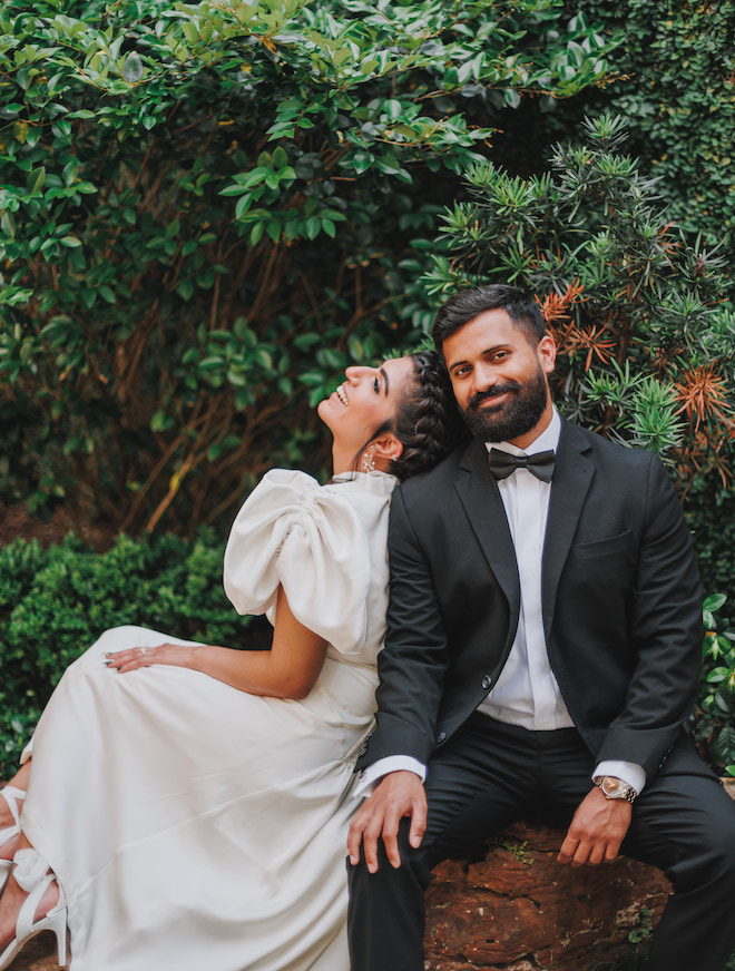 The bride leaning on the grooms shoulder as he smiles.