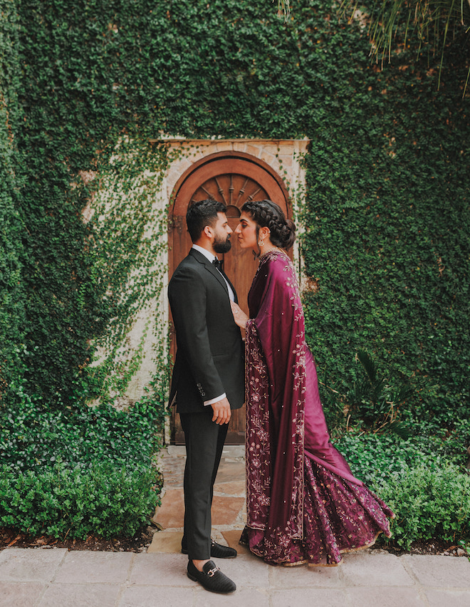 The bride and groom facing each other in front of a ivy-filled wall for their engagements at The Bell Tower on 34th.