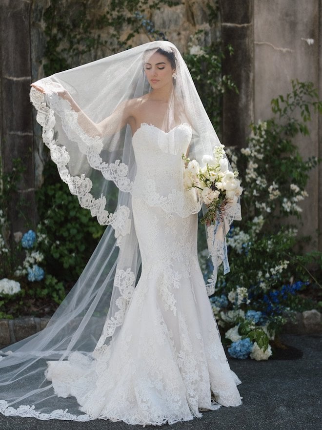 A lace strapless gown with a sweetheart neckline with a cathedral-length veil from the Spring 2024 Anne Barge Collection.