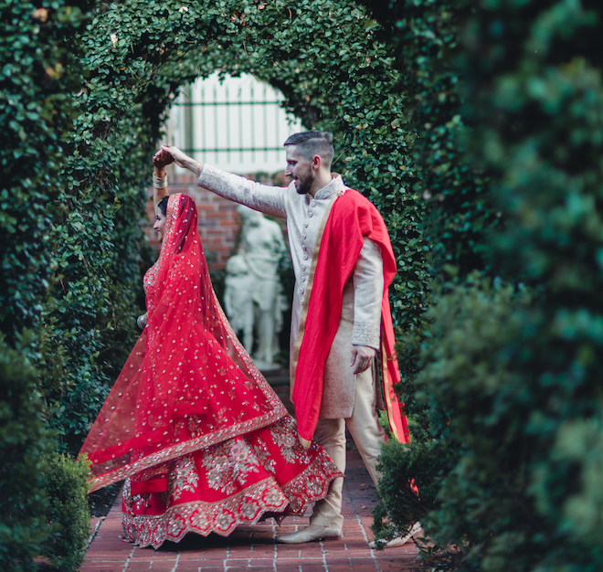 The groom twirling the bride in front of a arch of greenery.