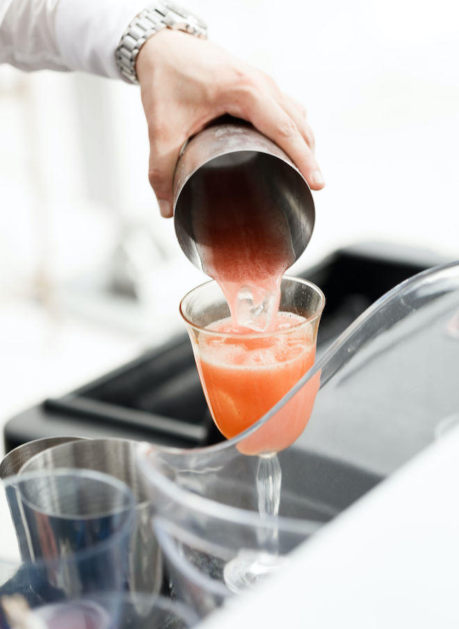 An orange cocktail being poured into a glass from a cocktail shaker.