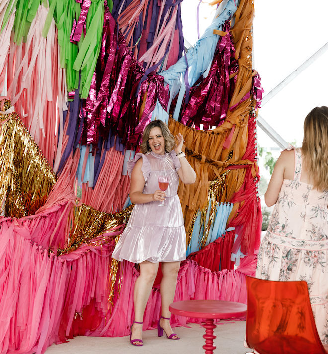 A woman smiling standing in front of a colorful backdrop of streamers.