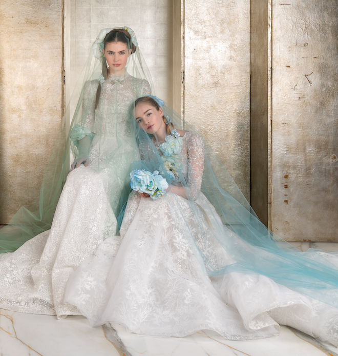 Two brides wearing lace gowns with blue and green veils.